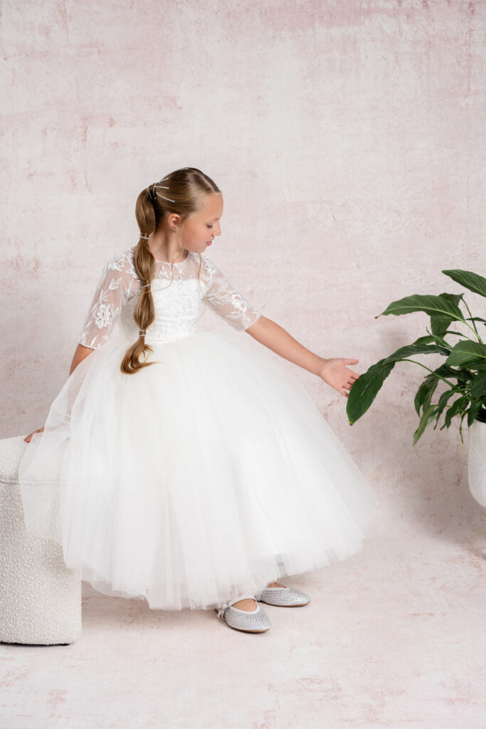 Agirl sitting gracefully in a beautiful handmade Communion dress, showcasing intricate detailing and elegant craftsmanship.